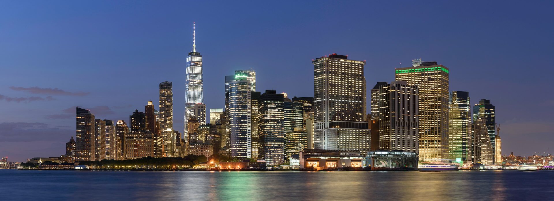 Lower Manhattan seen across the water from Governors Island at dusk, the financial district skyline lit against an evening sky.